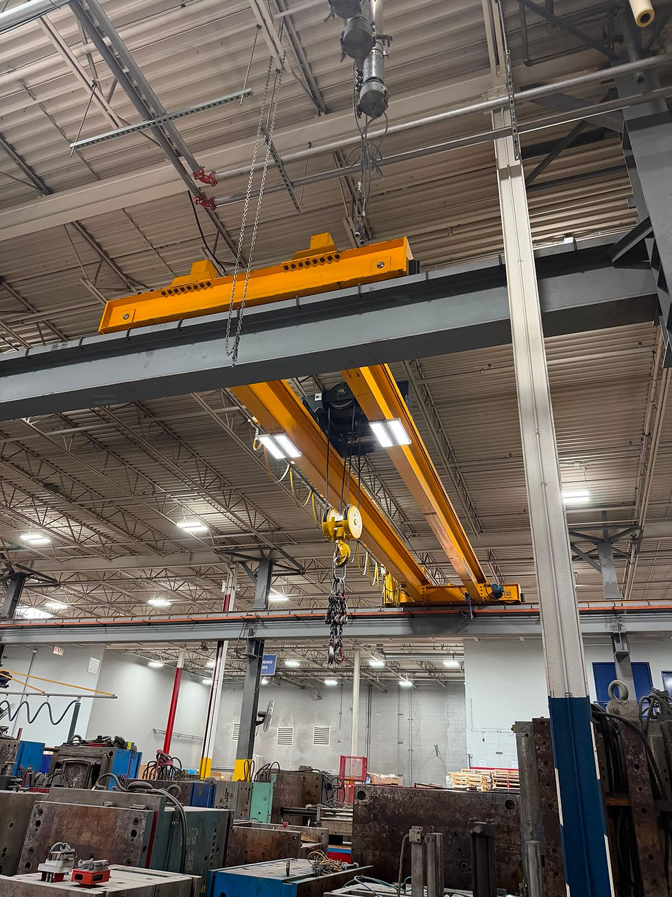 Overhead yellow crane and hoist system inside an industrial factory bay, wide landscape shot showing crane beam, hook, and shop floor below.