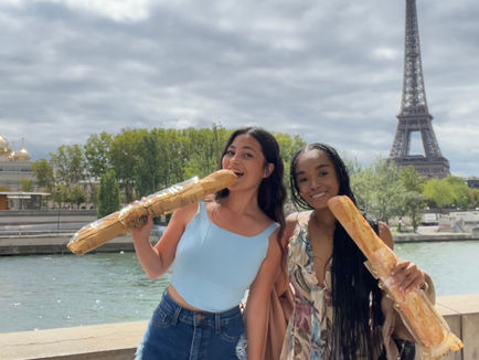 two girls eating giant baguettes in front of the river and the eiffel tower in paris, france