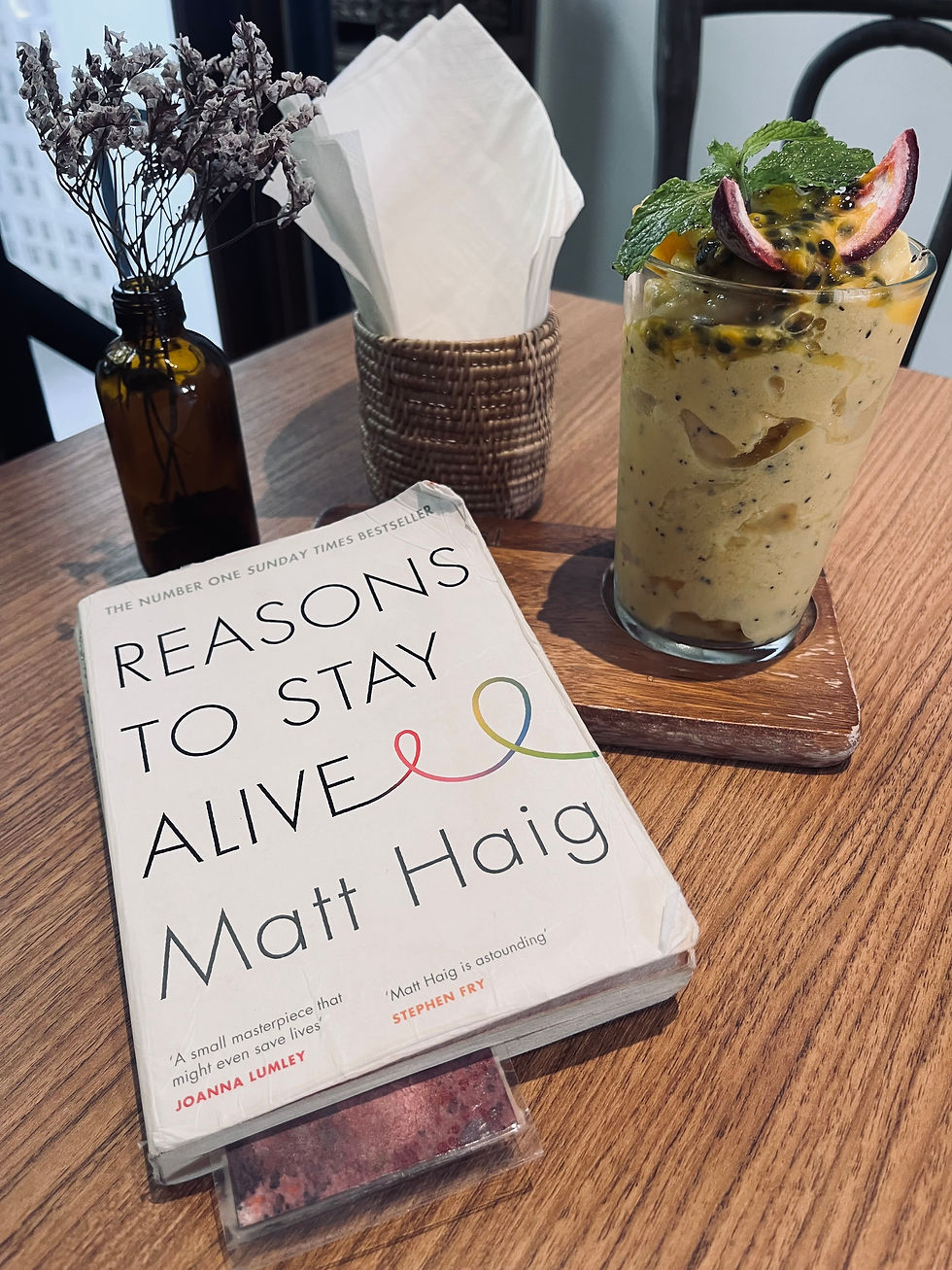 smoothie à la passion et livre Reasons to stay alive de Matt Haig sur une table dans un café