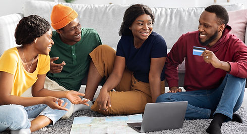 Happy young black friends sitting on floor at home, using laptop, holding credit card, loo