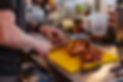 Man cutting roasted BBQ chicken on a yellow chopping board.