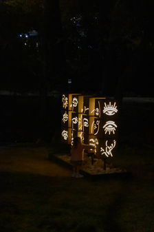 A young child approaches an outdoor sculptures of illuminated faces on turnable cubes