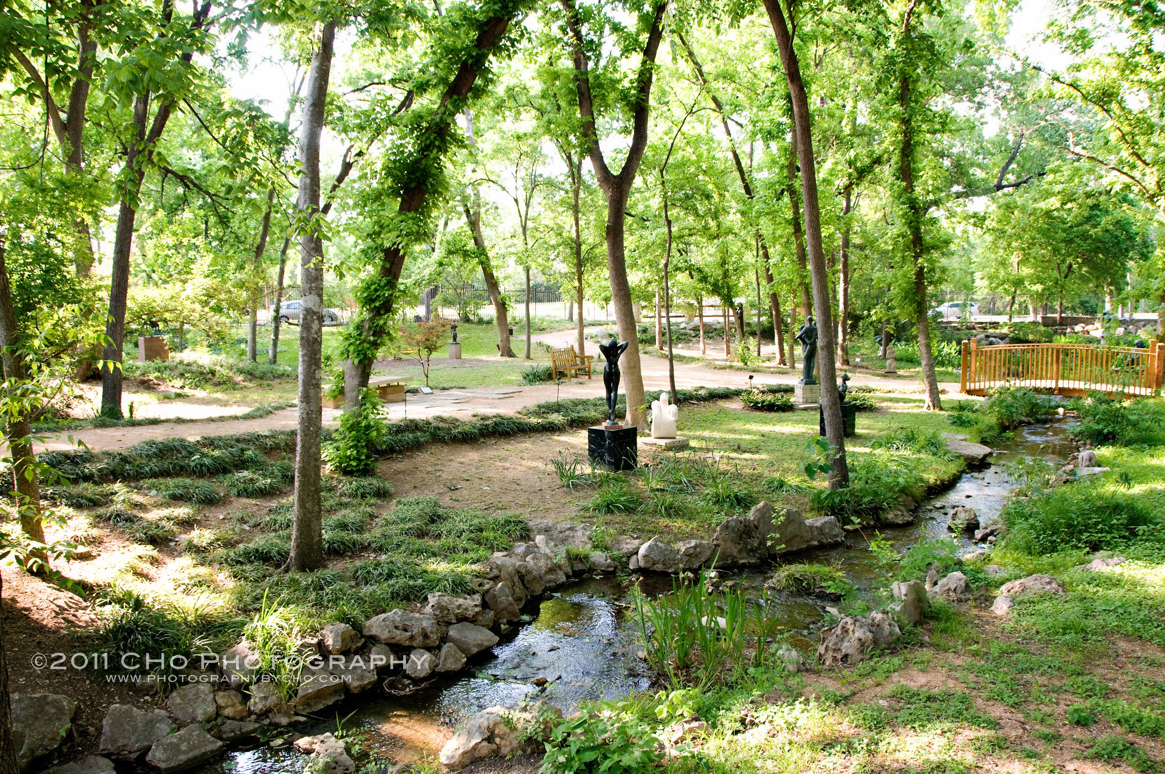 A garden featuring many trees, a stream, and bronze sculptures