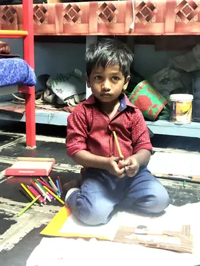 Young orphan boy in India kneeling, holding a colored pencil
