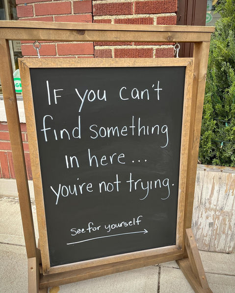 Wood chalkboard sign on sidewalk reads "If you can't find something in here... you're not trying! See for yourself." 