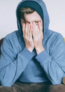 Young man covering his face in a gesture of exhaustion.