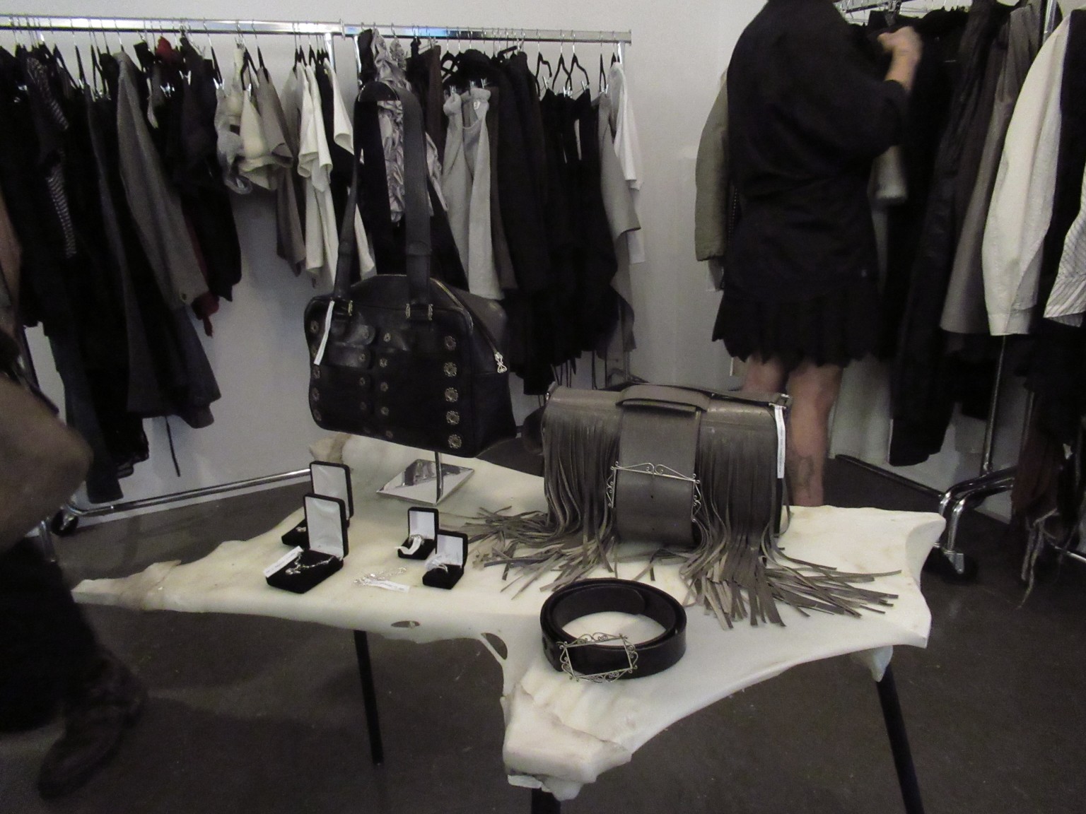 Bags, jewellery and a belt are arranged on an irregular white table among racks of clothing in the LDF showroom.