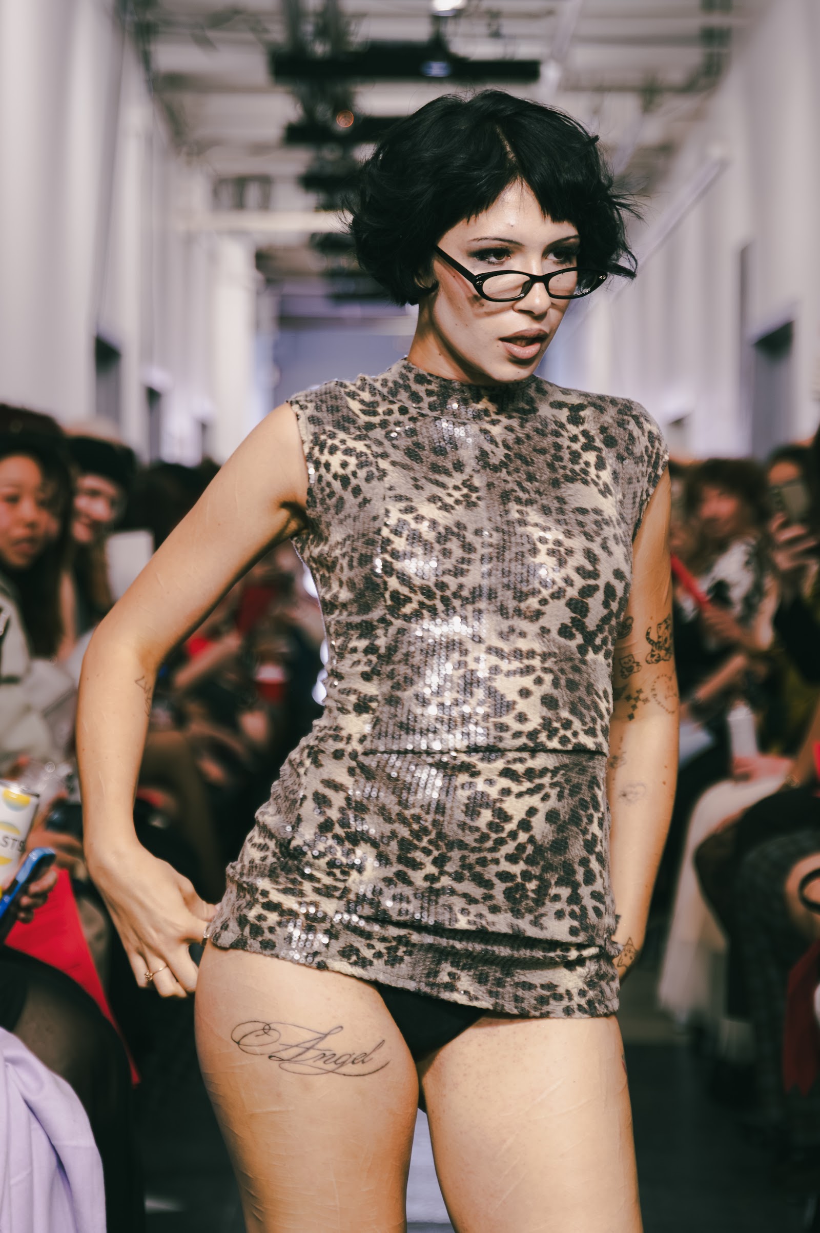 A model wearing glasses and a sequinned leopard-pattern sleeveless top walks close to the audience at ON SHOW.