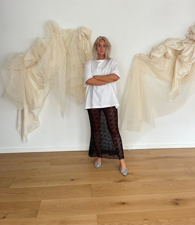 Floral artist Stine standing in front of a wall with an art installation.