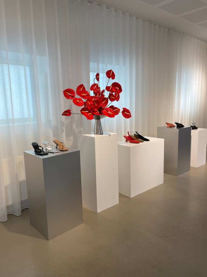Red floral arrangements on white pedestals, STUDIO FLØR exhibition of shoes and fashion.