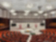 Spacious governmental assembly hall with orange seats, large circular arrangement, chandeliers, and Turkish flags. Text: "Egemenlik Kayitsiz Sartsiz Milletindir."