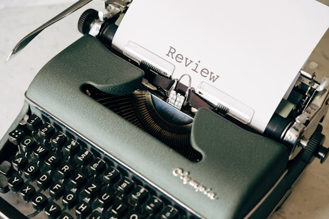 Close-up of a vintage green typewriter with "Review" typed on paper. The setting is a light desk, exuding a nostalgic, focused mood.