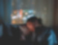 A person relaxes on a couch, gazing at a smartphone. Blurred city lights glow in the background, creating a calm, reflective mood.