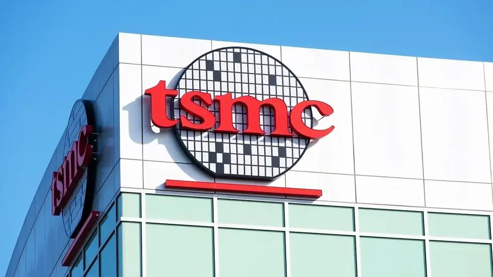 Building with large red "tsmc" logo on a white wall against a clear blue sky. Glass windows below add a modern look.