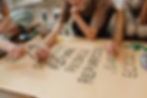 Hands paint "Refuse, Reduce, Repurpose, Reuse, Recycle" on poster. Art supplies and green leaf drawing visible in creative setting.
