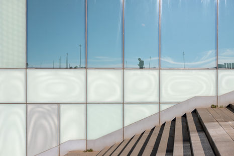 Grid of glass facade panels with sunlit stair shadows and soft reflections.