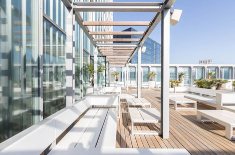 Modern rooftop terrace with pergola beams, benches, timber decking, and adjacent glass facade.