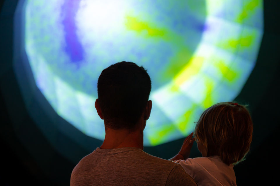 Back view of a man and child looking at a colorful projected circle.