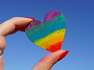 Rainbow love heart being held by a hand.