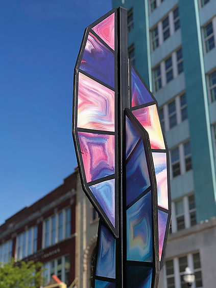 A tall sculpture with feather like panels that look like stained glass protruding from a center steel support.