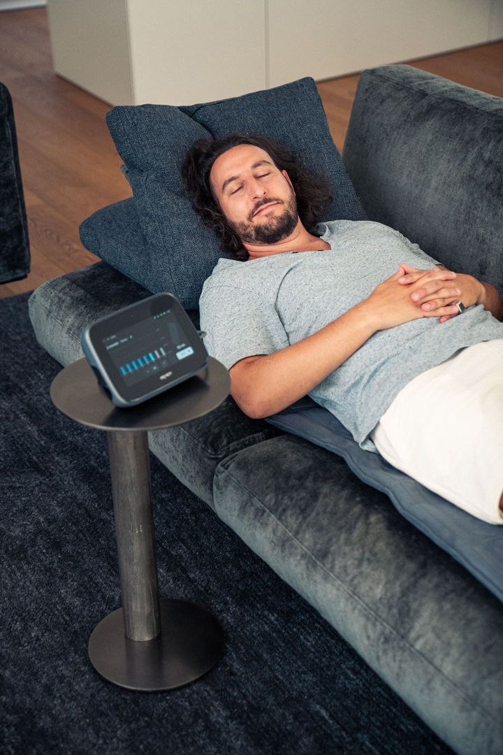 Mies makaa sohvalla Bemer -verisuoniterapia patjalla otamassa Bemerverisuoniterapia hoitia Bemer EVO hoitolaittella