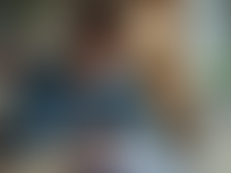 eye-level view of a student writing in a notebook with a laptop and study materials on the desk