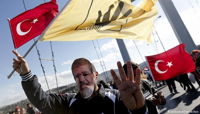 Man wearing Morsi mask and waving Rabia sign and the Turkish flag