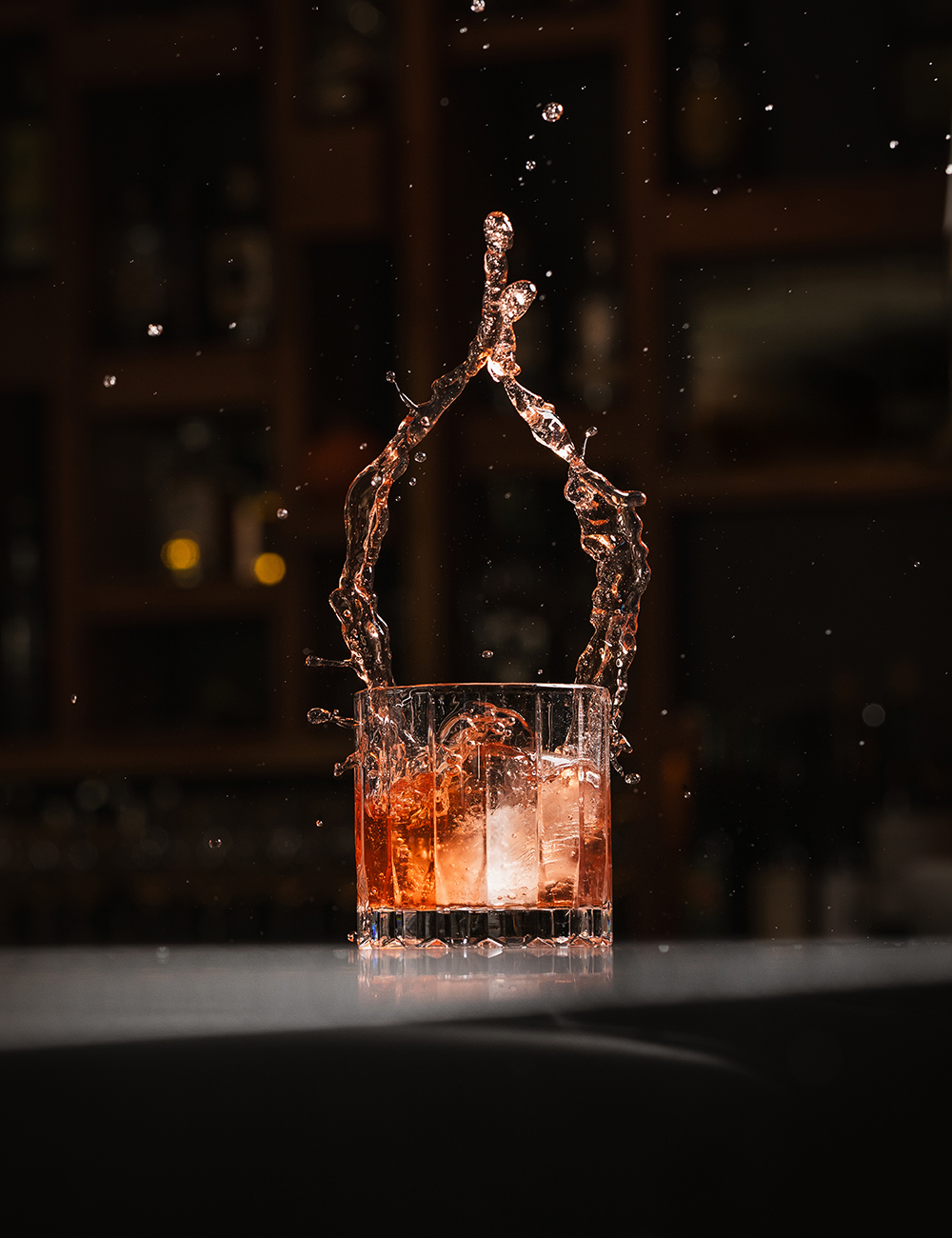 “Whiskey cocktail on a bar top with warm reflections.”