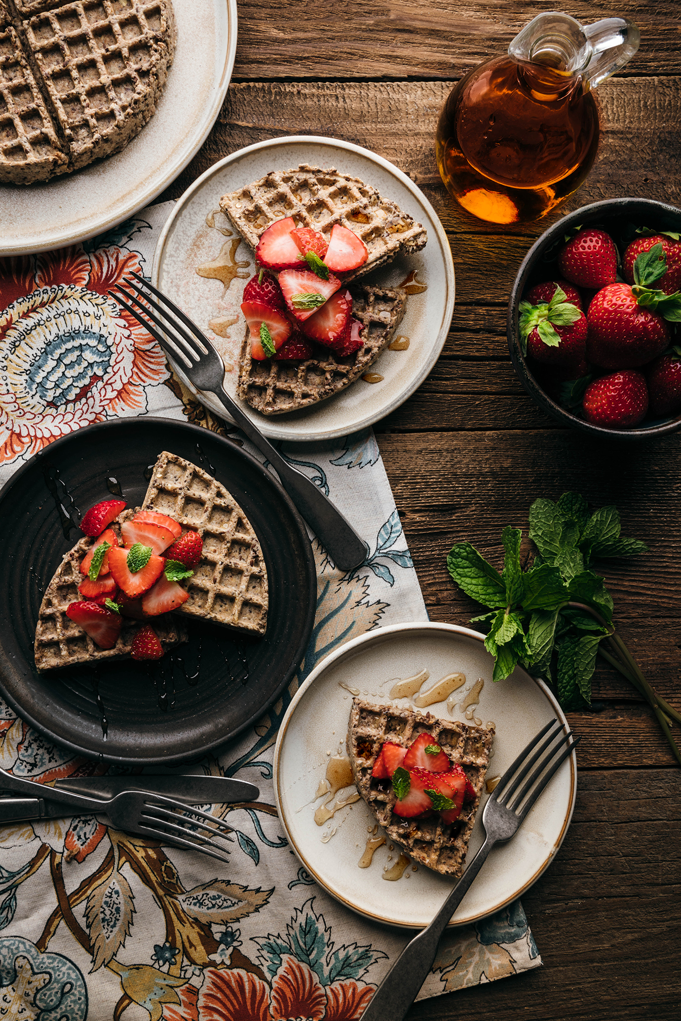 “Waffles topped with strawberries on a table with fresh berries.”
