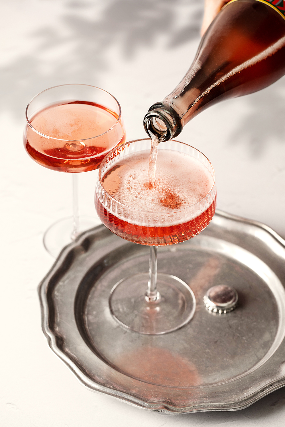 “Sparkling rosé being poured into coupe glasses on a metal tray.”