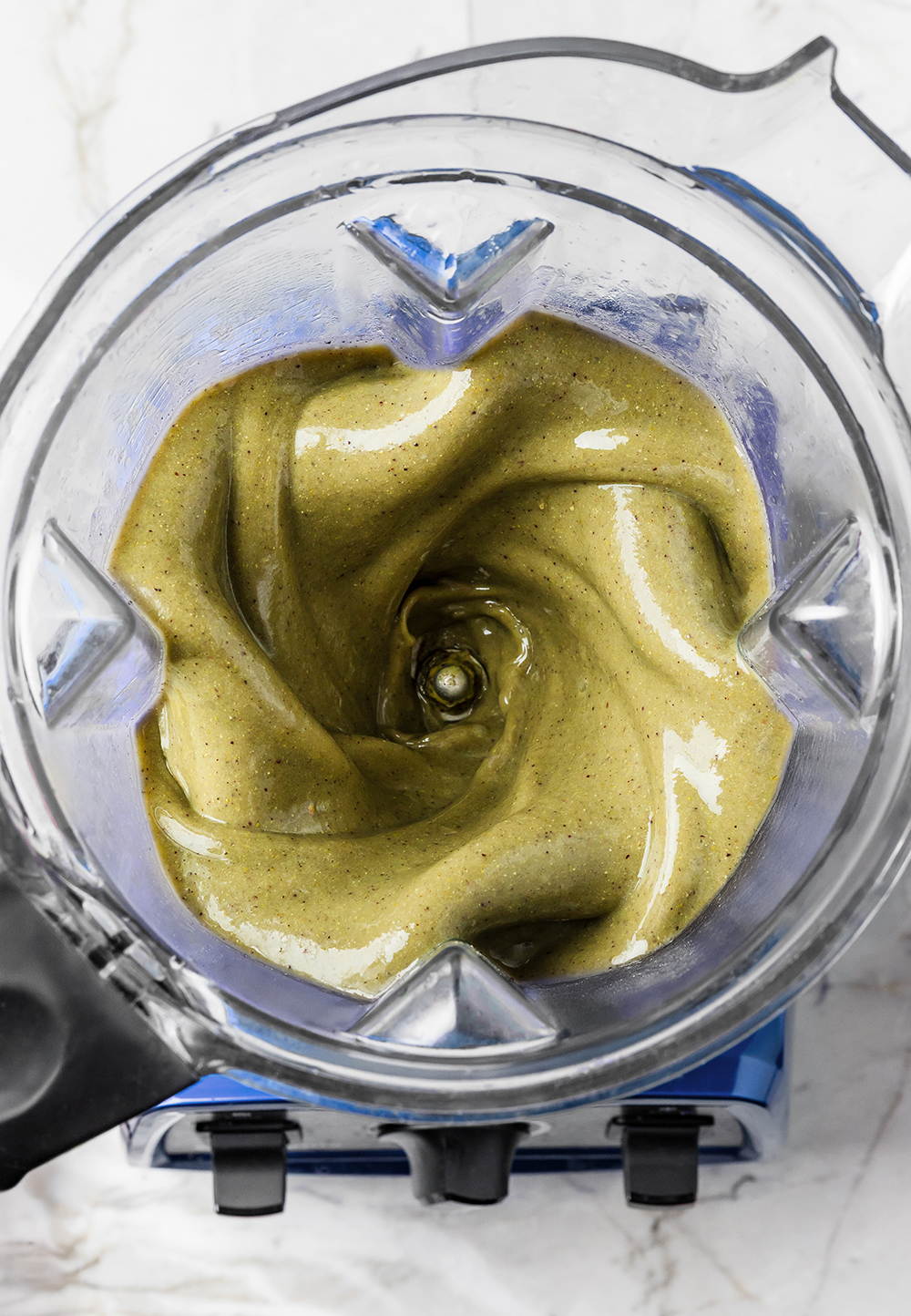 “Blender jar with thick green smoothie mixture swirling inside.”