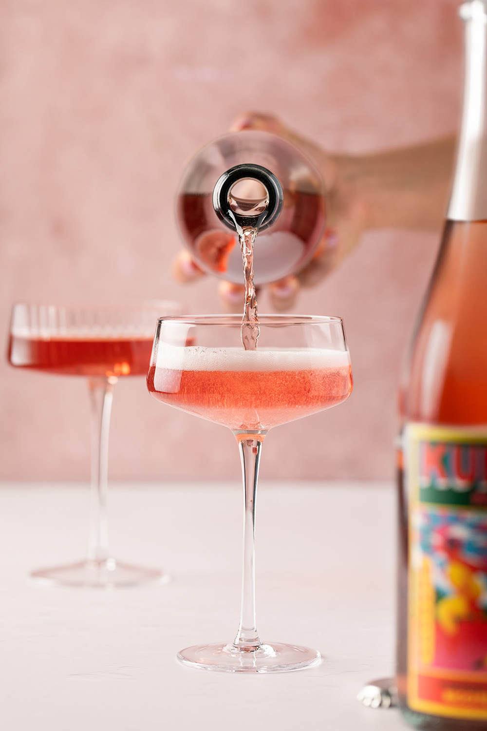 “Pink cocktail being poured into a coupe glass, drink photography.”