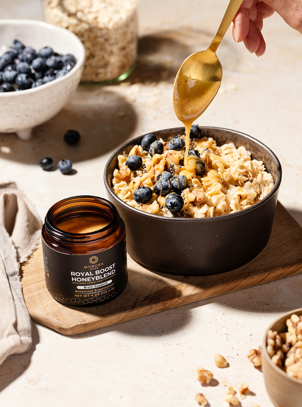 “Bowl of granola topped with blueberries with honey being poured, jar beside it.”