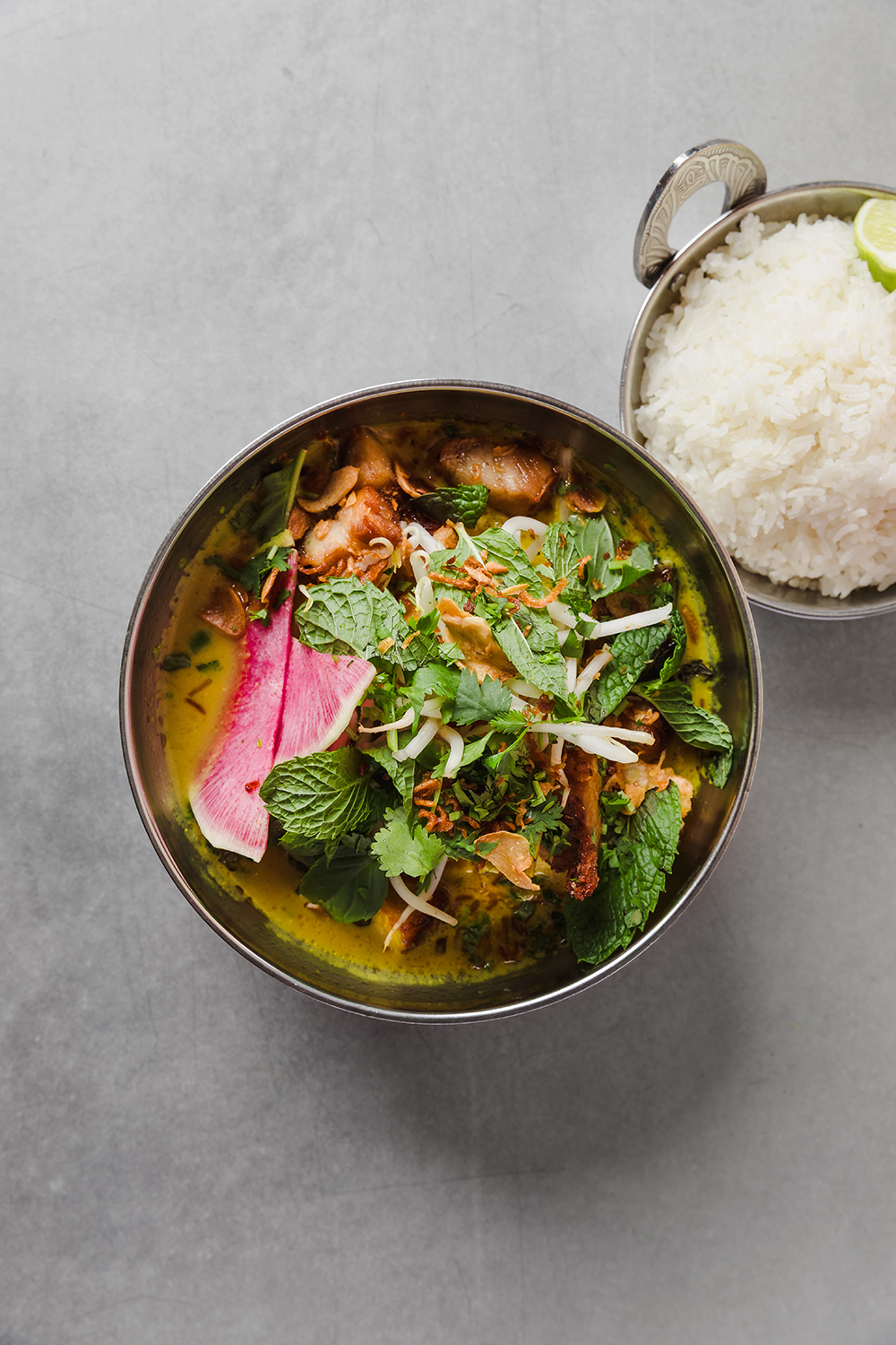 “Bowl of broth with sliced meat, herbs, and rice on the side.”