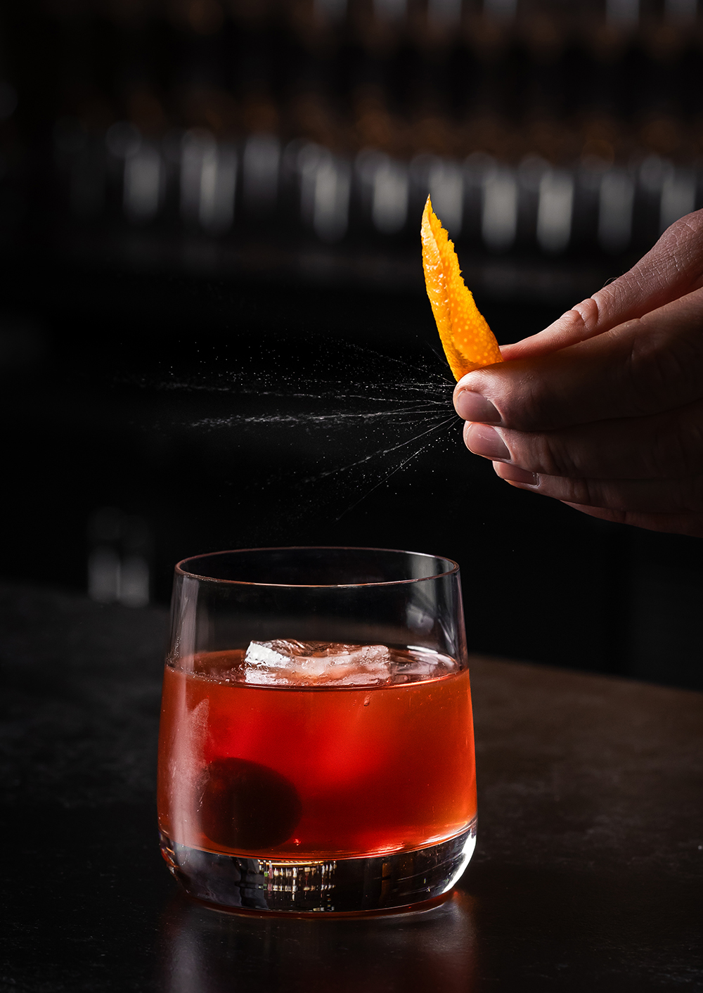 “Red cocktail in a rocks glass, dark bar background.”