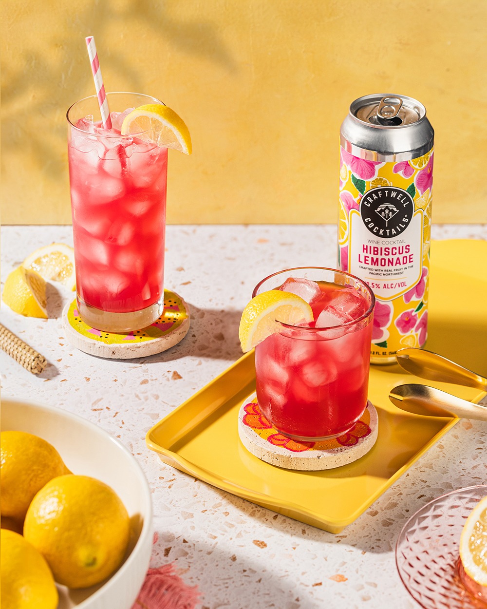 “Two red iced drinks with citrus garnish and a canned cocktail on a yellow tray.”