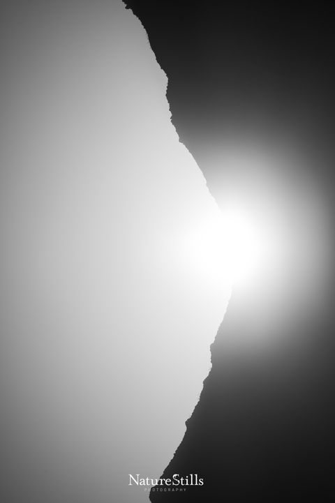Monochrome image of the sun rising behind a mountain ridge, creating a striking divide of light and shadow.
