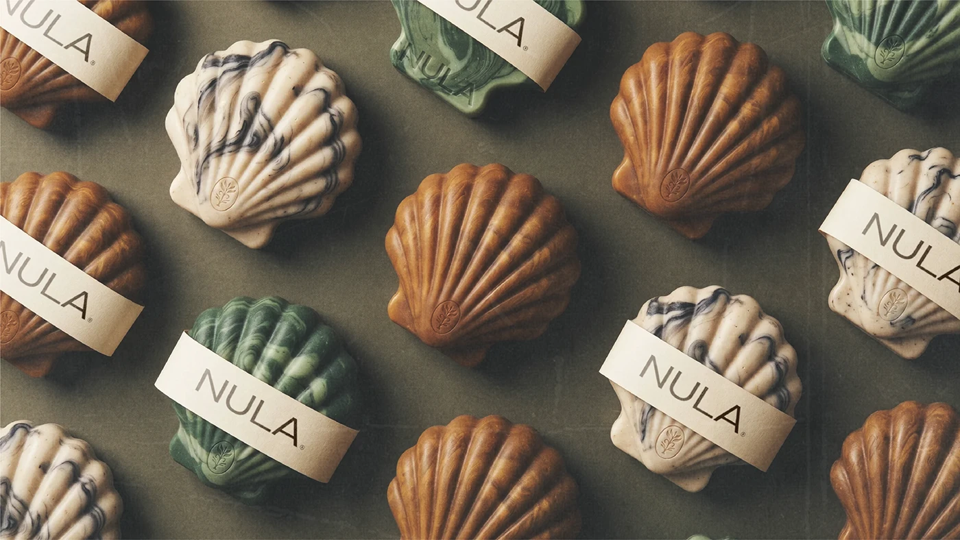 NULA shell-shaped organic soaps arranged in earthy brown, green, and cream tones with minimalist branded paper bands.