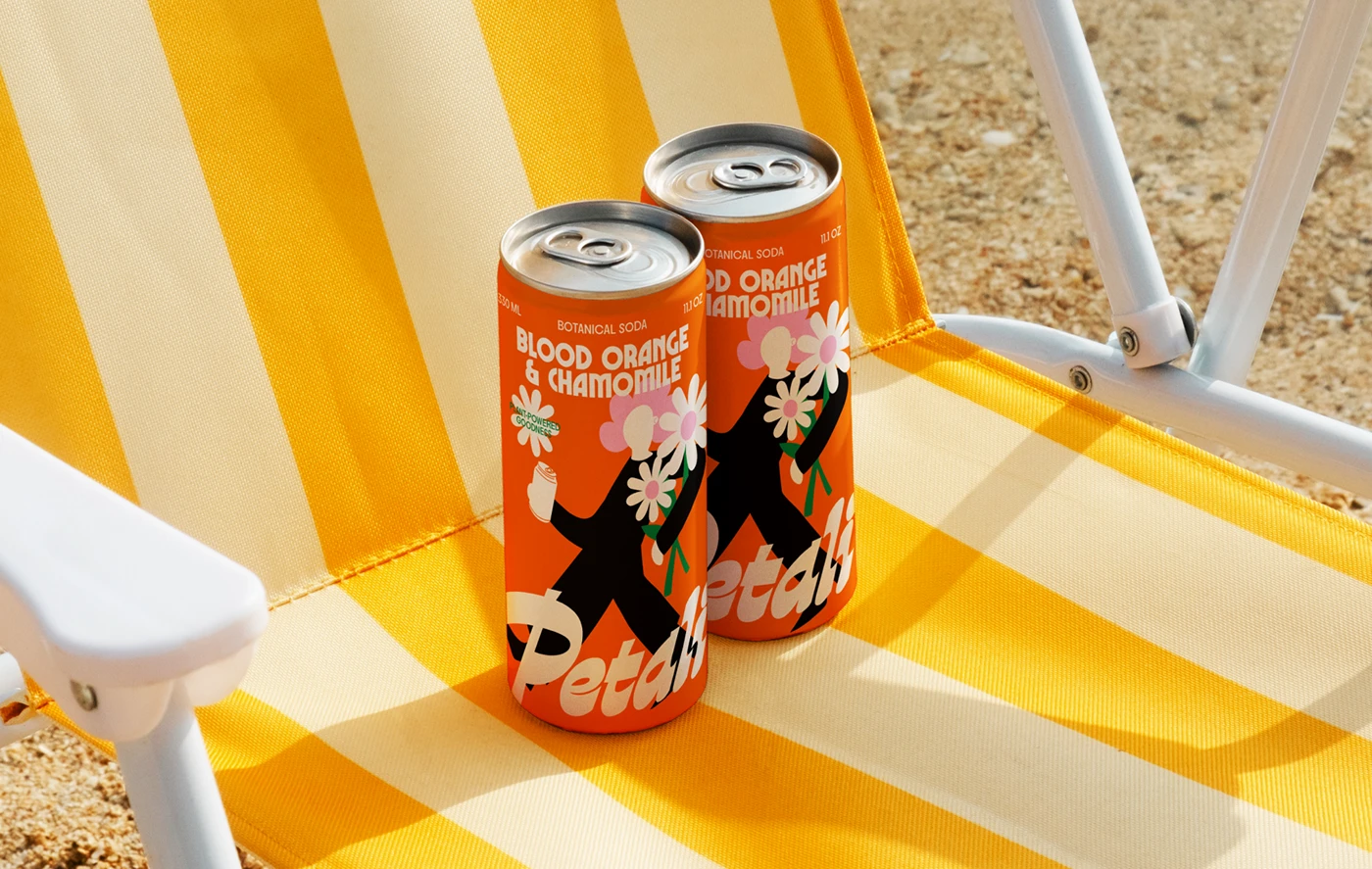 Petali Soda cans resting on a yellow-striped beach chair—vibrant beverage packaging design showcasing retro typography and summery lifestyle branding.