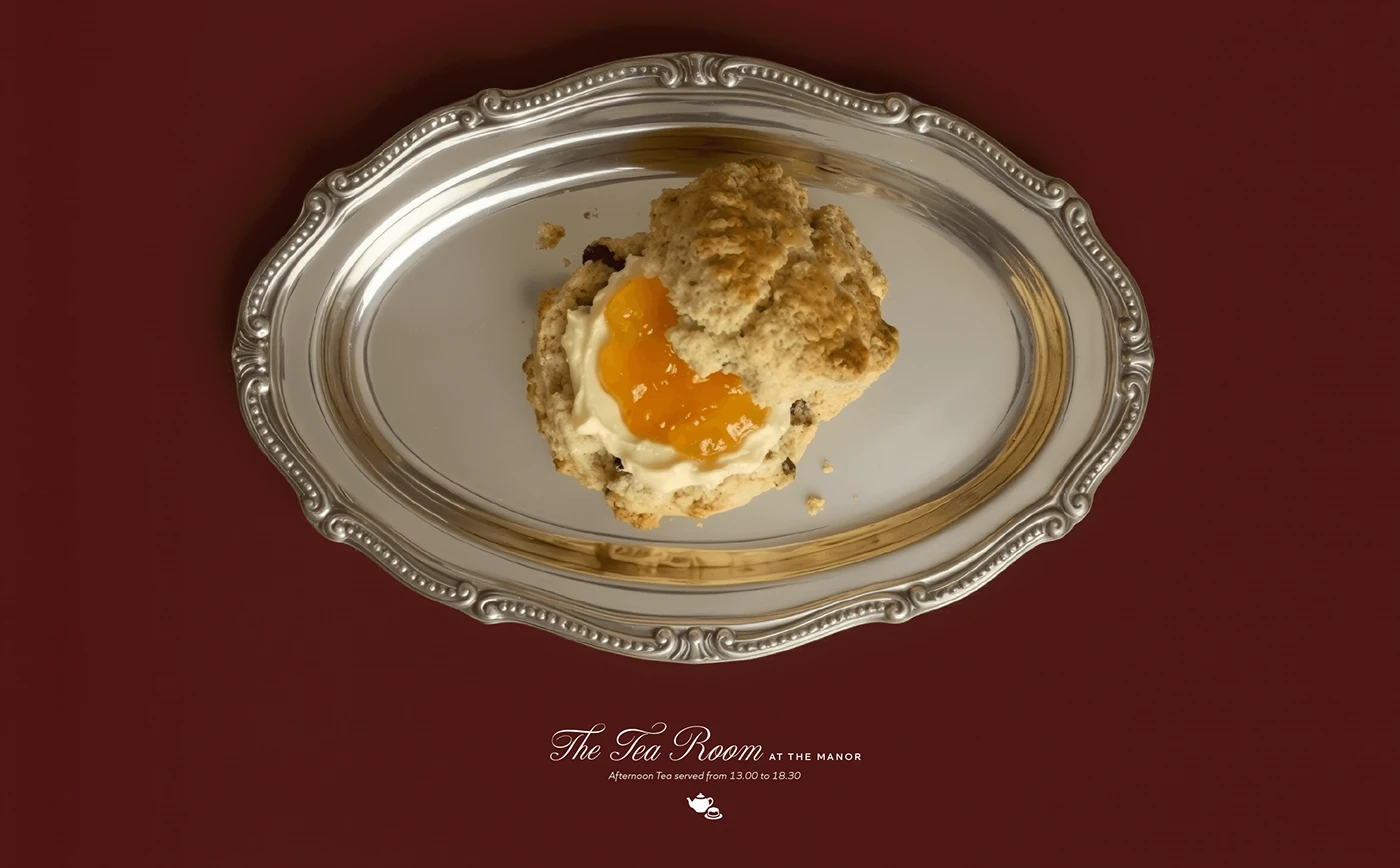 Marlow & Bromwell Manor afternoon tea branding with fresh scone topped with clotted cream and orange marmalade served on ornate silver tray against deep burgundy background, featuring The Tea Room at the Manor text