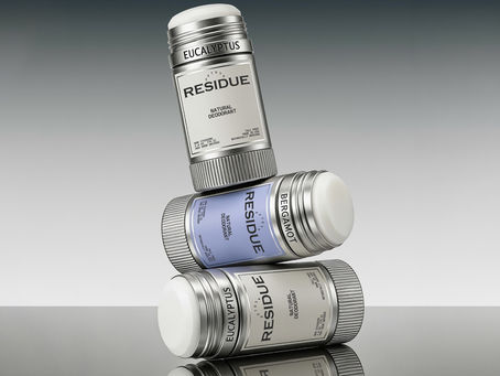 Three natural deodorant sticks stacked diagonally, showcasing silver packaging, white and powder blue labels, exposed deodorant formula, and engraved fragrance names.