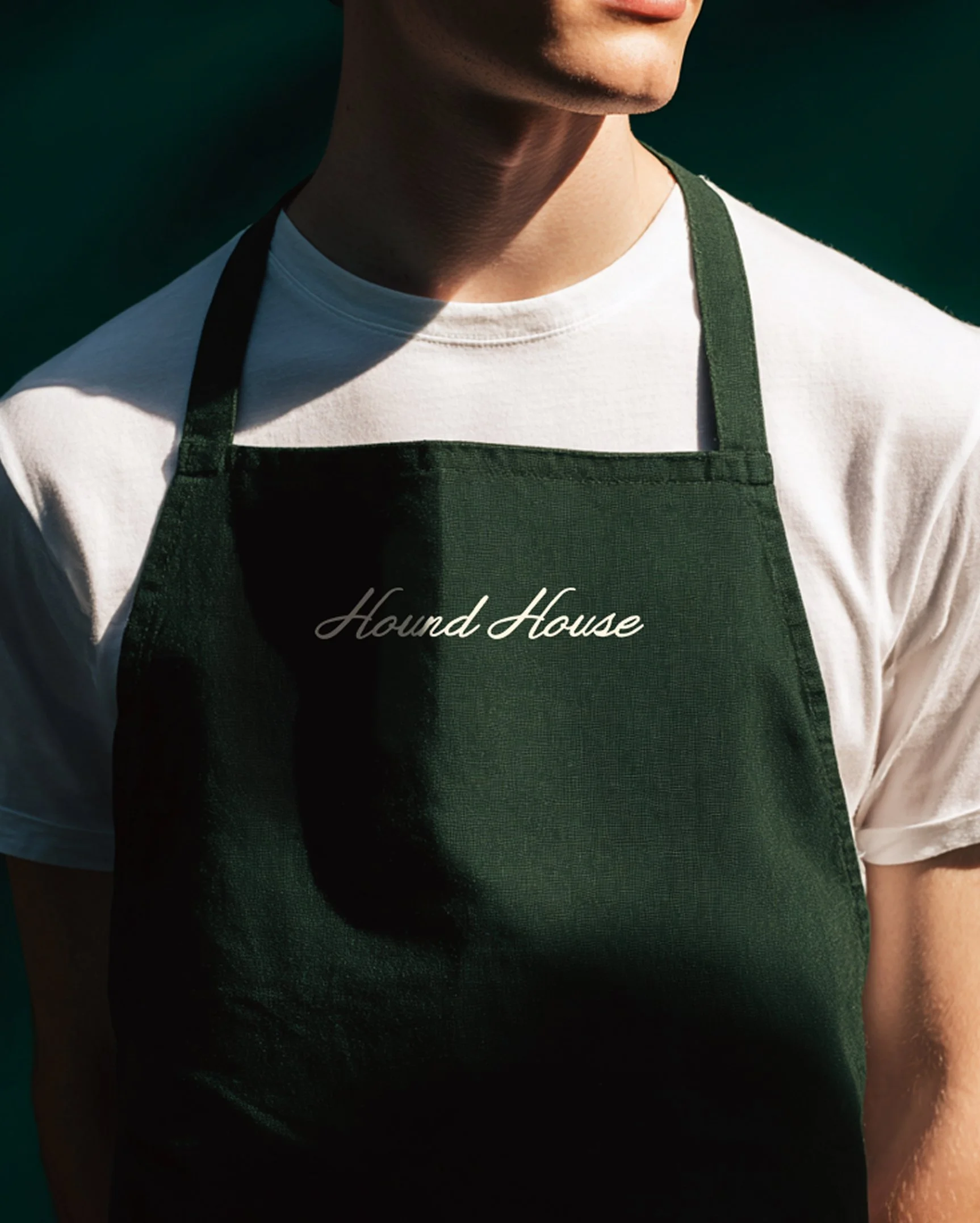 Staff apron embroidered with the Hound House script logo, showcasing branded apparel for a private pet social club and hospitality environment.