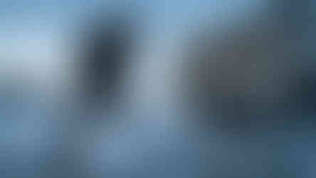 Man drilling into a frozen lake beside an ice house trailer featuring the North Country Outdoors logo.