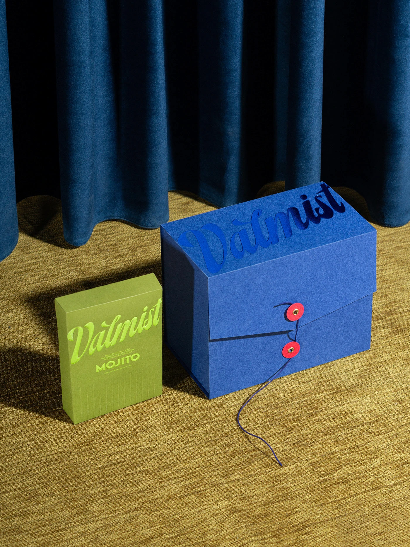 Valmist Mojito RTD package displayed next to a blue storage box with button-and-string closure, styled against deep blue curtains.