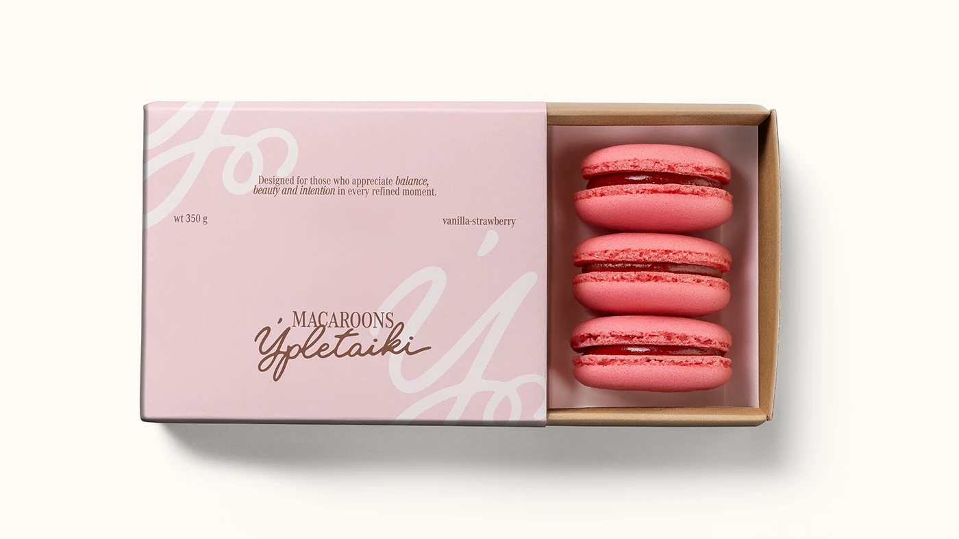 Blush pink Ypletaiki macaron box packaging with brown script logo and vanilla-strawberry macarons displayed in a minimalist premium confectionery presentation.