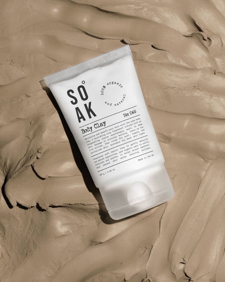 White Soak Body Clay skincare tube with black minimalist typography placed on a textured beige clay background.