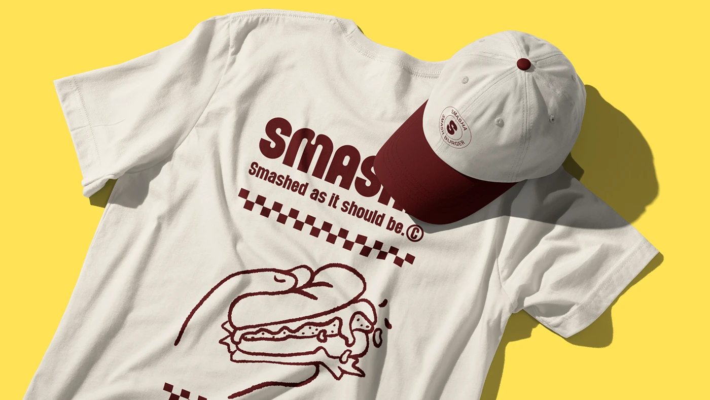 Flat-lay of Smasha branded merchandise including a cream t-shirt and matching cap with retro typography and illustrated burger graphic on a bright yellow backdrop.