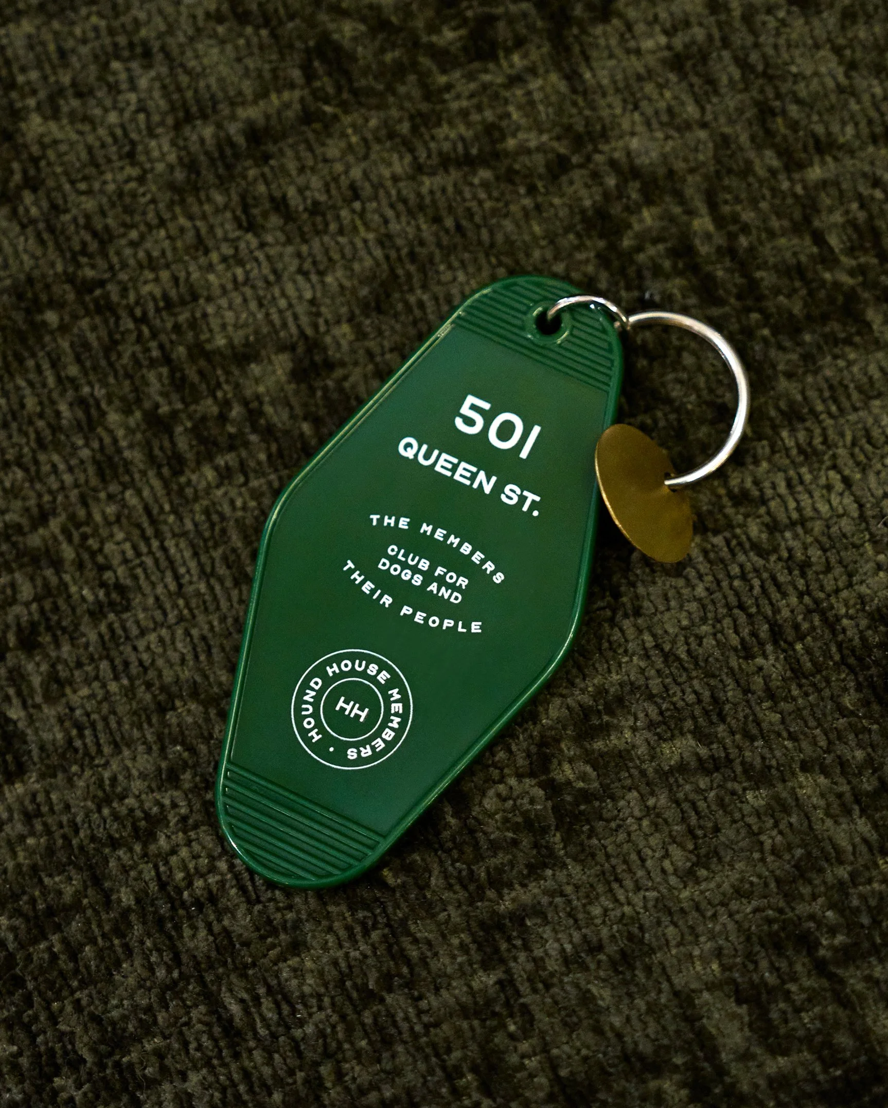 Green hotel-style keychain printed with Hound House member messaging, representing a private dog social club and pet hospitality brand identity detail.