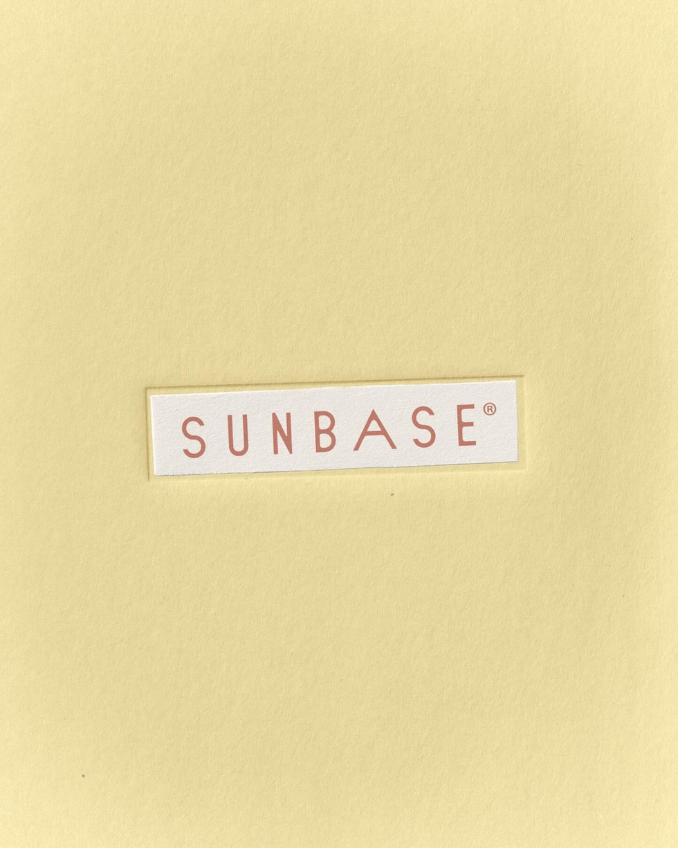 Sunbase logo printed on textured card over soft yellow background, minimalist skincare brand identity and typography design