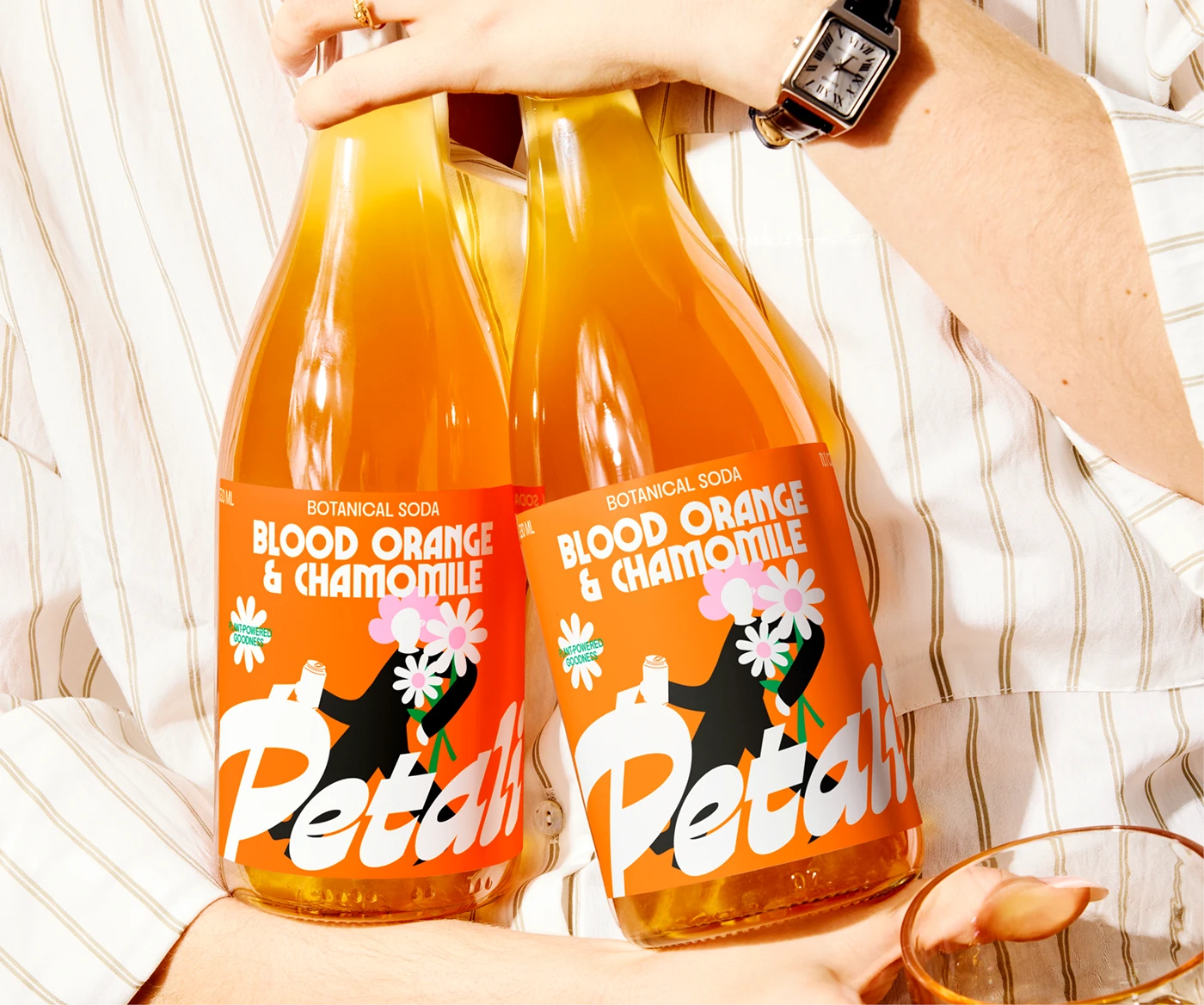 Petali Soda glass bottles labeled Blood Orange & Chamomile held in hand—botanical soda packaging design with groovy typography and dopamine color palette.